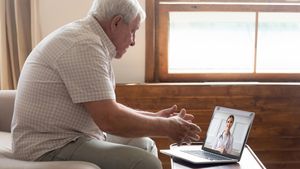 An older man is sitting with a laptop and conducting a telehealth visit with a provider
