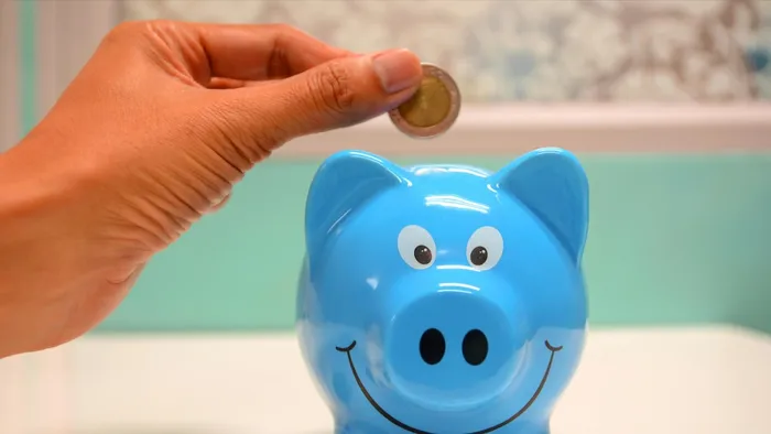 Person inserting a coin into a blue piggy bank.