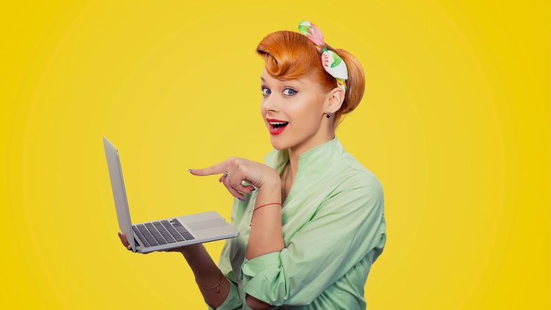 A woman wearing spring colored attire is standing holding and pointing at the screen of a MacBook managed by Jamf.