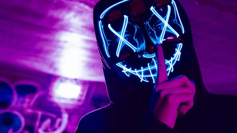 Masked figure wearing an LED mask with one finger over their lips