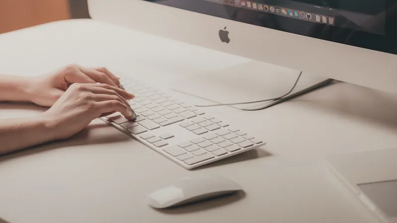 Person sitting at a desk, typing, using a Mac device.
