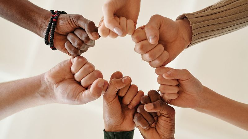 Hands from different ethnicities formed into a fist and united together in support.