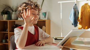 Student raising hand looking at iPad on desk at home.