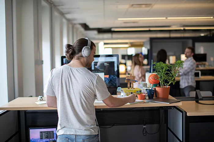 Jamf IT professional wearing headphones works at a standing desk with a Mac in a modern open office.