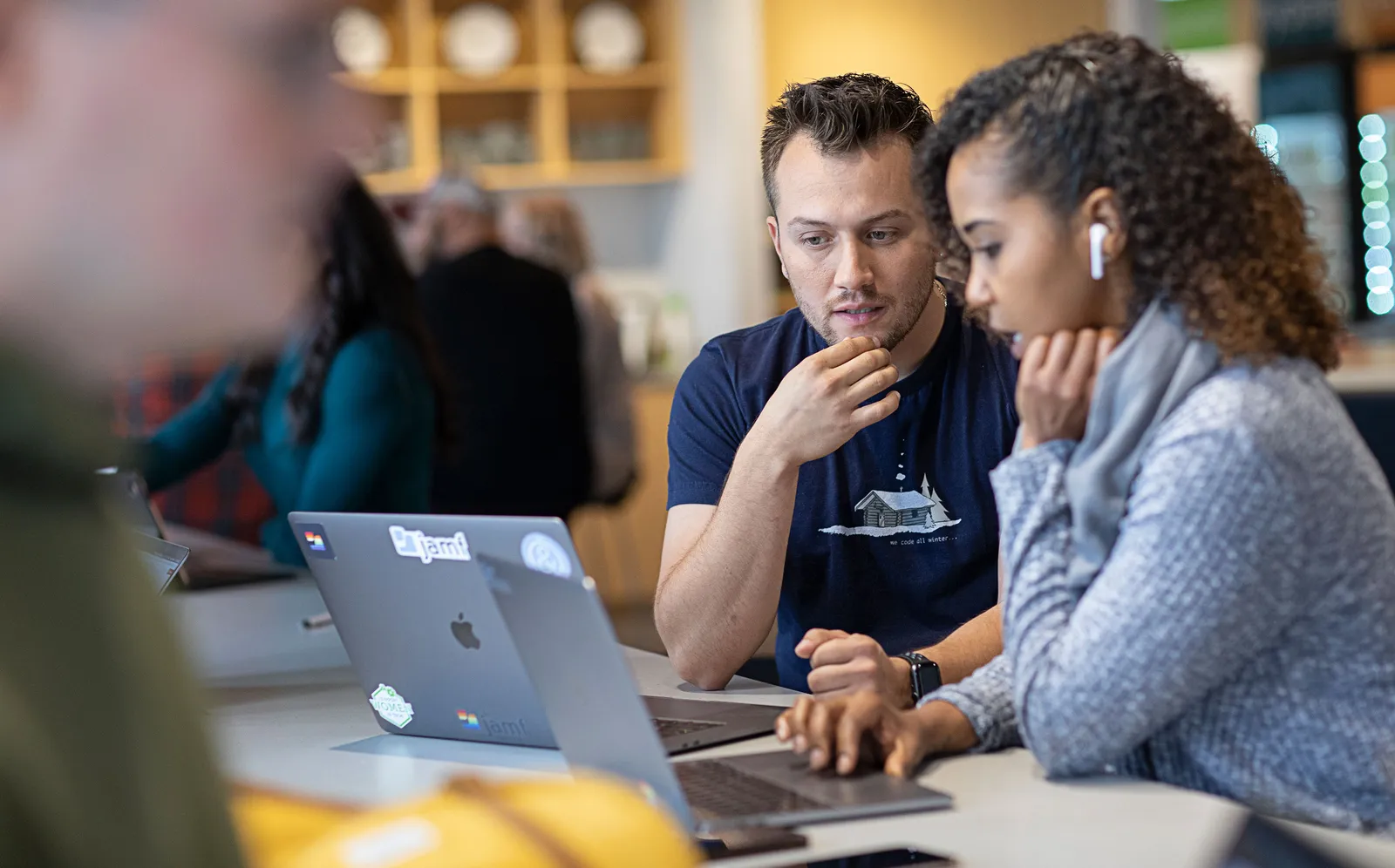 A man and a woman sitting at a desk with two MacBooks