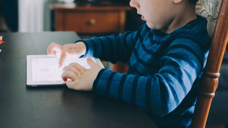 child sits at desk interacting with iPad