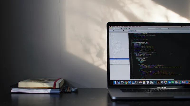 A Jamf MacBook Pro sitting on a desk, displaying PHP code. To the left of the computer are several pencils and a stack of notebooks.