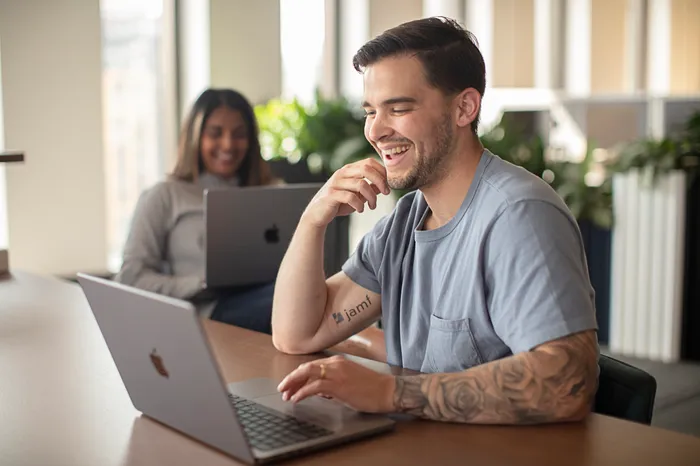 Two Jamfs laugh together as they work on their company-issued MacBooks.